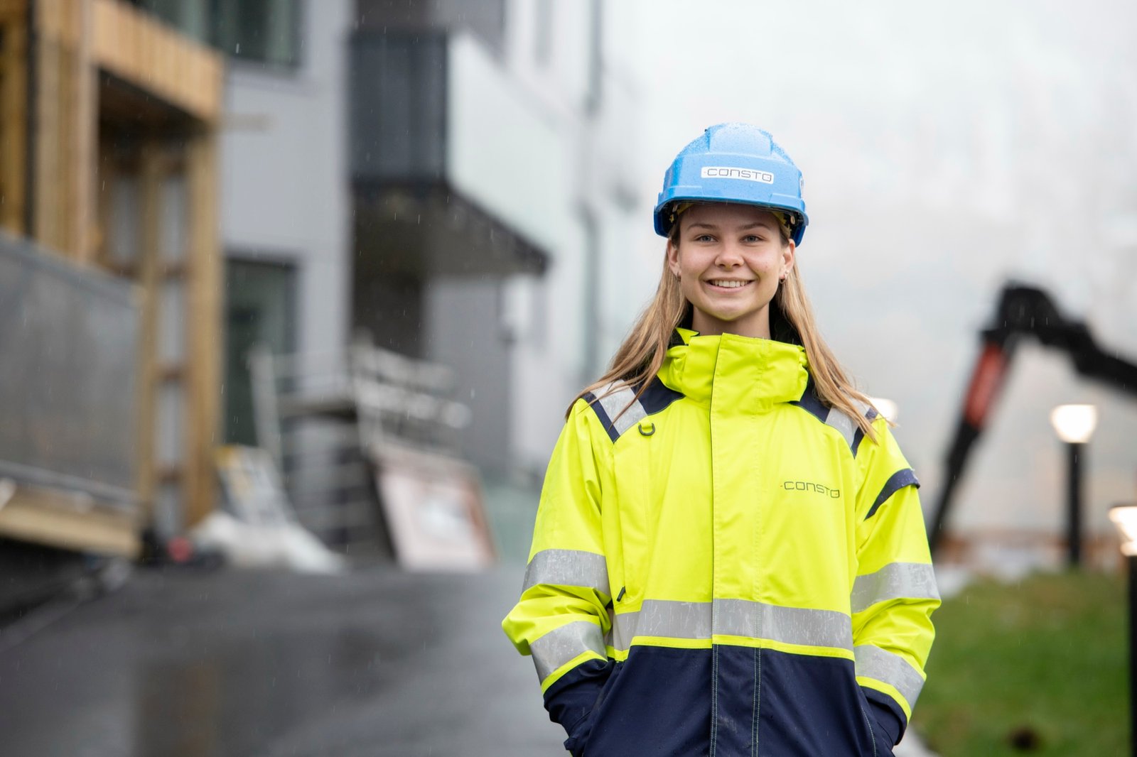 Smilende Consto-medarbeider i refleksjakke og hjelm på byggeplassen